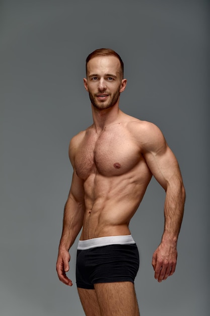 Young male athlete posing Handsome athletic male power guy Fitness muscular person Young athlete showing muscles in the studio posing shirtless on gray background
