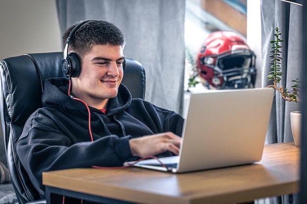 A young male athlete sits in front of a laptop in his room