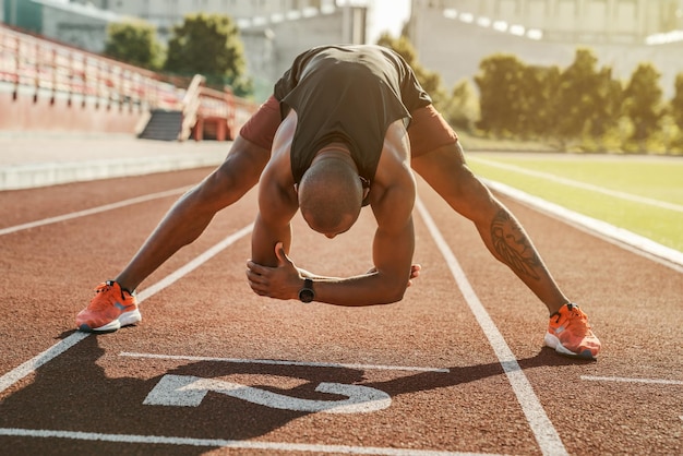 Young male athlete standing on the running track while stretching his body before workout