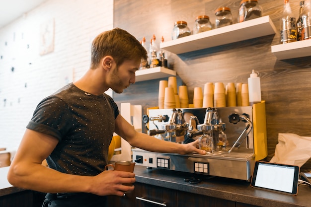 若い男性バリスタは、コーヒーマシンの近くで飲み物を作ります。