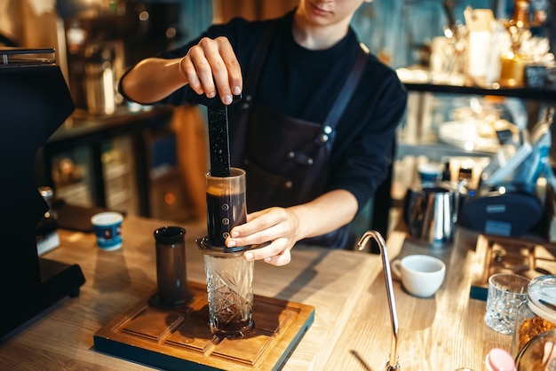 Young male barista makes fresh espresso in cafe