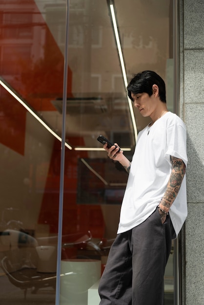 Photo young male barista with tattoos waiting outside the coffeehouse before opening and using smartphone