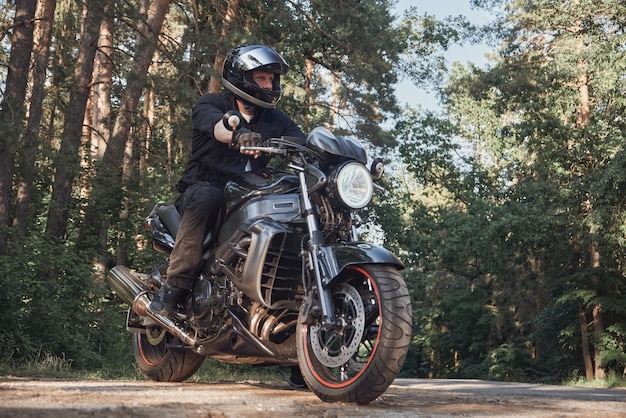 Young male biker in a helmet travels on a motorcycle alone on a road in the forest