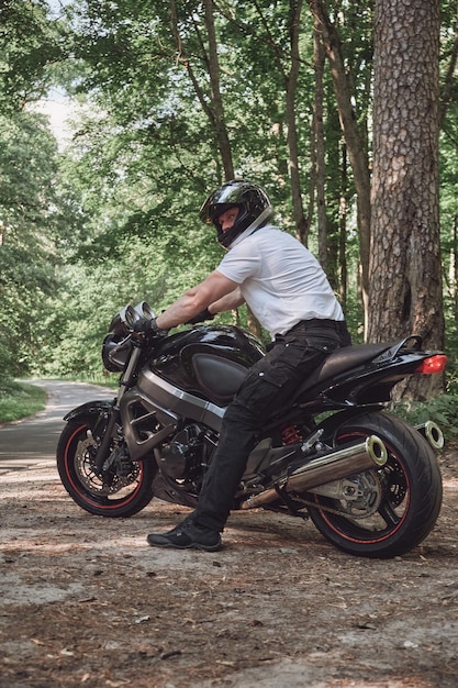写真 ヘルメットをかぶった若い男性バイカーは、森の中の道路を一人でバイクで旅行します