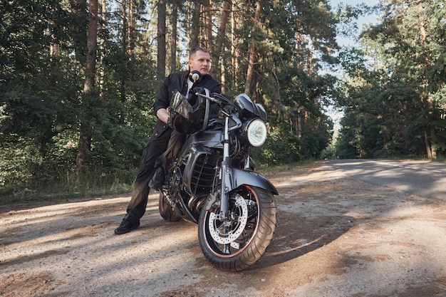 Giovane motociclista maschio viaggia su una moto da solo fermato sul lato di una strada forestale