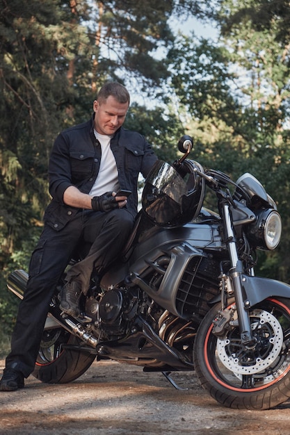 Young male biker travels on a motorcycle alone stopped and using a mobile phone on the side of a for