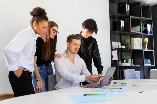 A young male boss shows information to his colleagues on a laptop screen