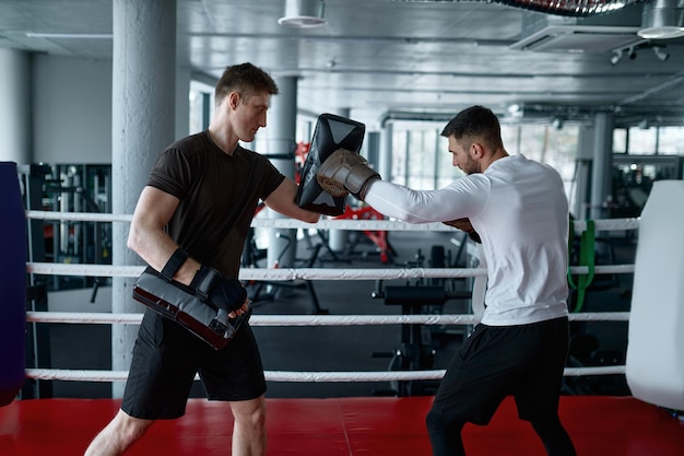 Young male boxer practicing with personal trainer during training session at gym