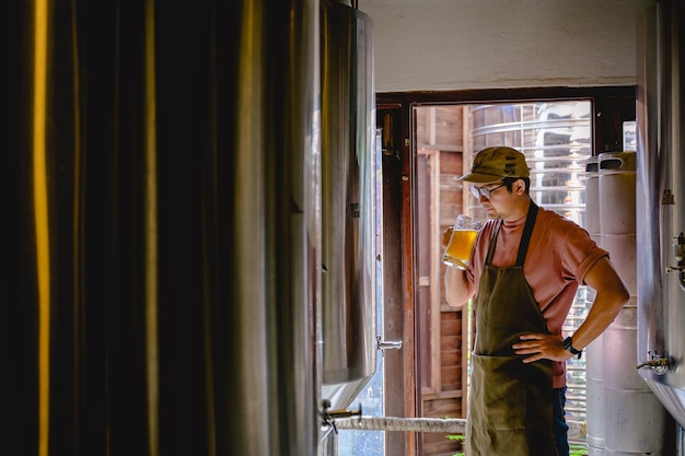 Young male brewer holding a glass of beer in hand Eating craft beer to check the taste and color of the beer in the craft brewery