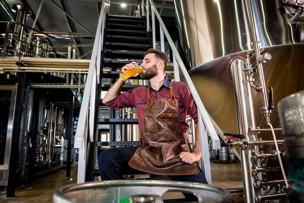 Foto giovane birraio maschio in grembiule in pelle nella moderna fabbrica di birra