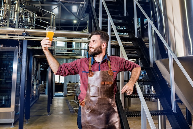 Young male brewer in leather apron at modern brewery factory