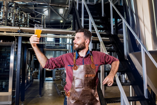 Young male brewer in leather apron at modern brewery factory