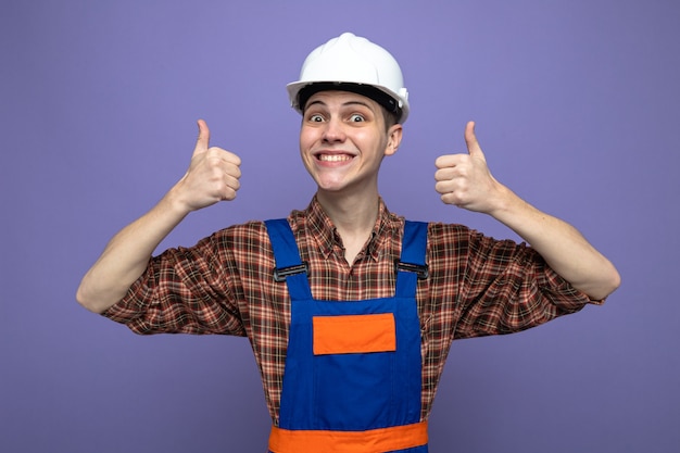 Young male builder wearing uniform isolated on purple wall