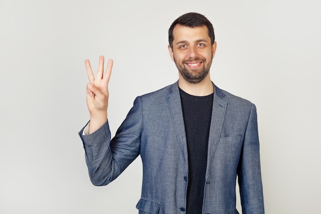 Il giovane uomo d'affari maschio con la barba che sorride mostrando le dita numera tre