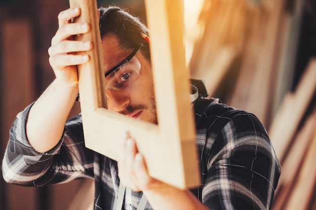 全体的に働いている若い男性の大工ビルダーは、ワークショップでフライス盤を備えた木製のバーに匹敵します、