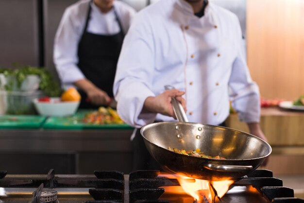 Young male chef flipping vegetables in wok at commercial kitchen