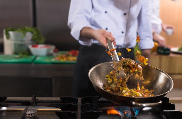 Young male chef flipping vegetables in wok at commercial kitchen