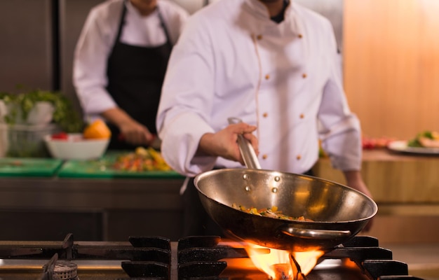 Young male chef flipping vegetables in wok at commercial kitchen