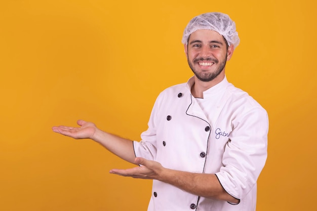 Young male chef under yellow background pointing to the side