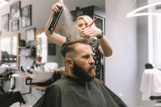 Giovane cliente maschio di un negozio di barbiere con acqua da una lampadina. taglio di capelli, barba styling.