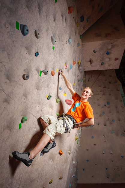 Young male climbing on practical wall in gym, bouldering