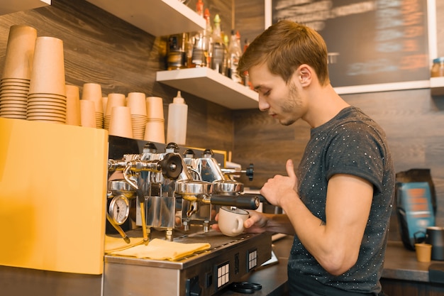 マシンでコーヒーを作る若い男性のコーヒーショップ労働者