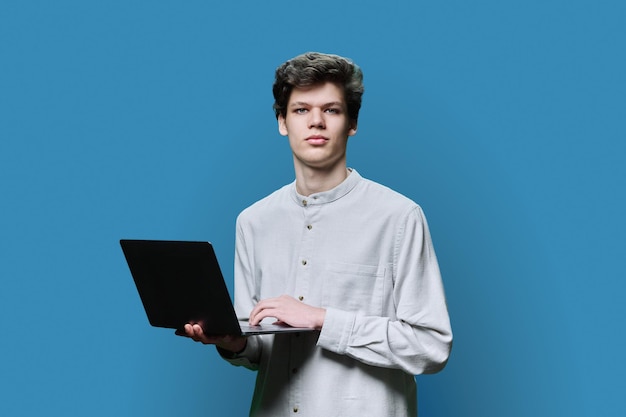 Young male college student using laptop blue background