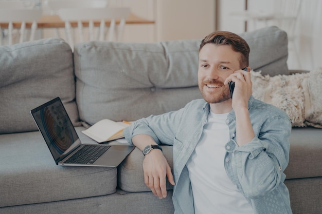 Young male company employee working remotely from home calling boss to tell good news