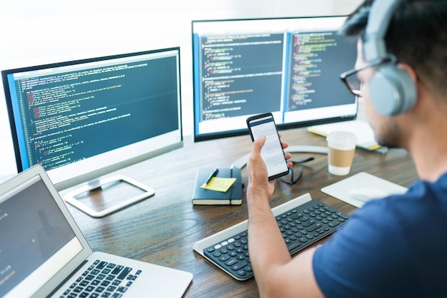 Young male computer science freelancer using smartphone at desk