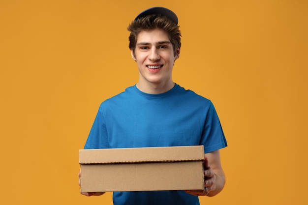 Young male courier in a blue uniform holds parcel in his hands