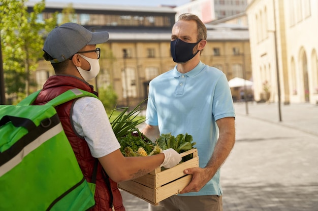 Young male courier in protective mask and gloves giving wooden b