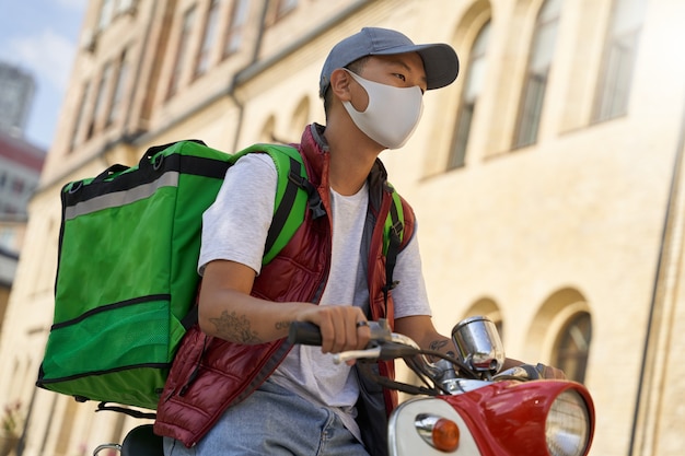 Young male courier with thermo bag wearing face protective mask