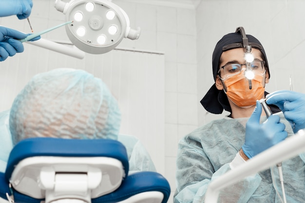 A young male dentist doctor treats a patient. Medical manipulations in dentistry, surgery. Professional uniform and equipment of a dentist. Healthcare Equipping a doctor workplace. Dentistry