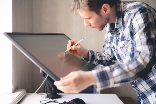 Молодой мужчина цифровой художник рисует краску на мониторе экрана компьютера в студии