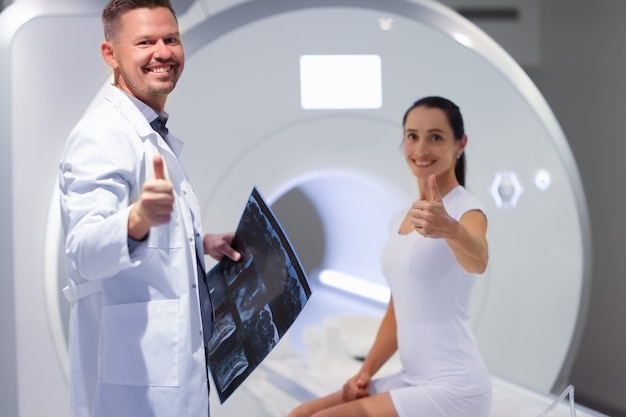 젊은 남성 의사와 여성 환자가 MRI실 자기공명영상에서 엄지손가락을 들고 있다