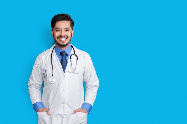 写真 青い壁に隔離されたポケットに聴診器と腕で笑っている若い男性医師。健康保険の概念。