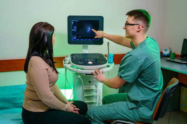 A young male doctor shows patient an ultrasound of the abdominal cavity Doctor explanes a woman analysis Cheerfull male medician with special equipment