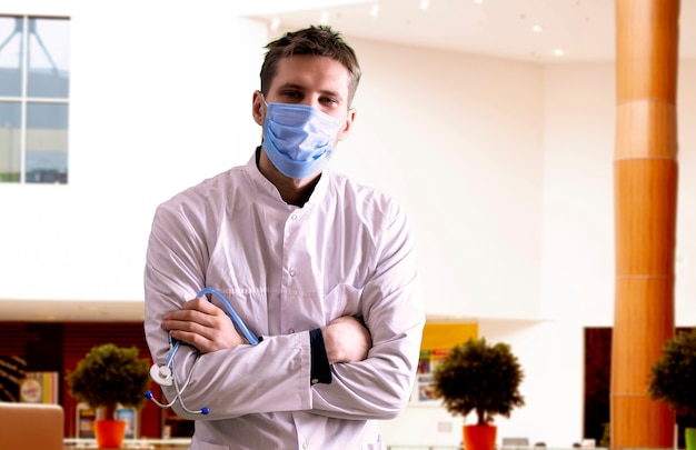 A young male doctor in uniform wearing the protective mask in hospital, medicine clinic