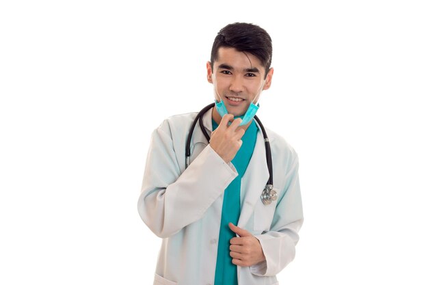 Young male doctor with stethoscope in uniform and mask posing isolated on white background