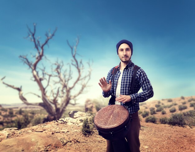 Young male drummer plays on wooden bongo drums in desert, musician in motion.