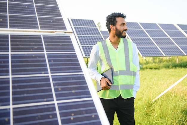 Young male engineer with tablet in hand standing near solar panels agriculture farm land with clear blue sky background Renewable energy clean energy