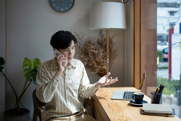 Photo young male entrepreneur sitting in modern workplace and talking on mobile phone.