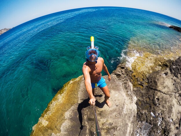 Young male explorer in adventure ready for snorkeling. Selfie shot at summer day at rock in the middle of the sea.