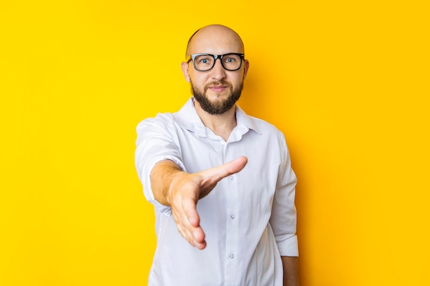 Young male extending his hand for a handshake greeting on a yellow studio background