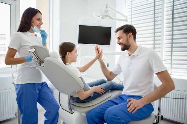 Young male and female dentists working with little child giving high five in dental office