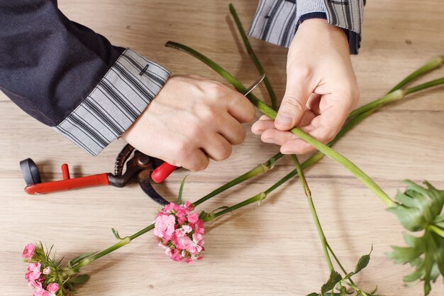 Молодой мужской флорист срезает цветы в цветочном магазине, крупным планом