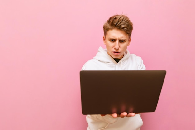 young male freelancer working on laptop with serious face isolated on pink background