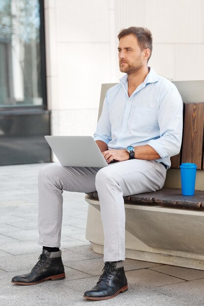 Young male freelancer working using laptop while sitting on the street