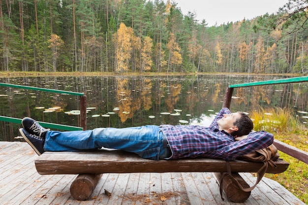 秋の森の湖の近くで休んでいる若い男性ハイカー