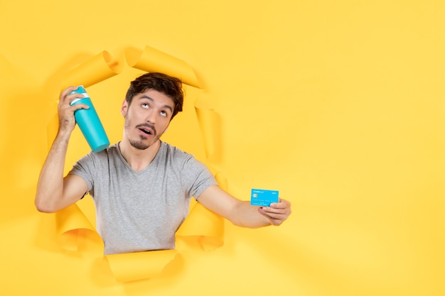 young male holding credit card and bottle on yellow background sale athlete